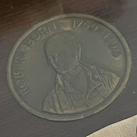 Close-up of a bronze Robert Burns medallion, 1759 to 1796, set into a dark tabletop.